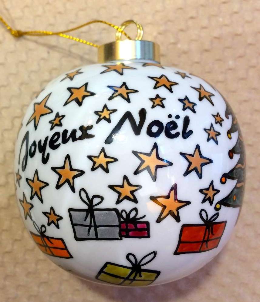 Boule de Noël en porcelaine personnalisée par un Joyeux Noël, des cadeaux, un sapin et des étoiles dans un style naïf.
